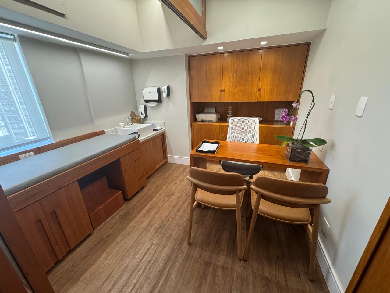 Sala de atendimento do consultório, com mesa de madeira e maca de exames